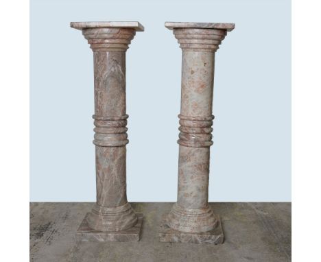 A pair of classical-style marble pedestal columns, each featuring a square top that rotates freely. The cylindrical columns a