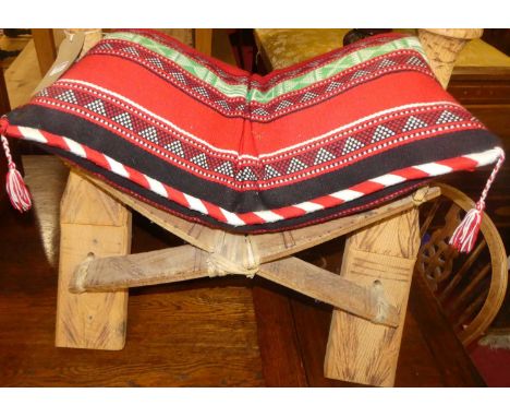 An Eastern line carved softwood camel stool, with Kelim cushion, w.60cm