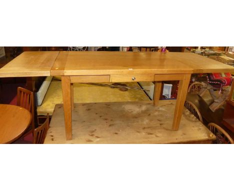 A contemporary light oak refectory table, having drawleaf end attachments, single frieze drawer, and raised on square cut sup