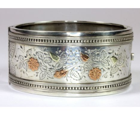 A Victorian hallmarked silver bangle with yellow and rose gold decoration.