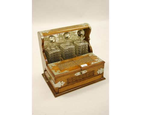 Edwardian oak and silver plate mounted three bottle tantalus, the bi-fold lid retaining the three hobnail and facet cut glass