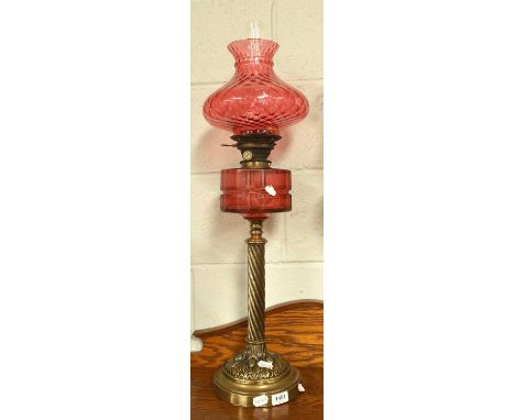 A Victorian Brass-Based Oil Lamp, raised on twist pedestal, with cranberry glass reservoir and quilted shade, no. 2 Hinks bur