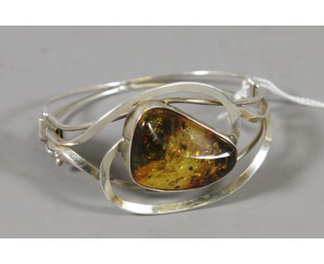 A ladies hinged openwork silver bangle set with a large natural amber specimen.