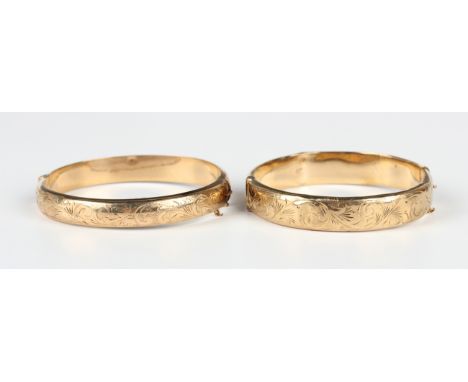 Two 9ct gold oval hinged bangles, each front with engraved decoration, on a snap clasp, London 1965 and Chester 1961, total w