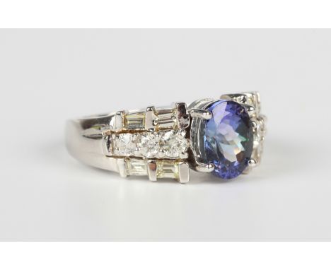 A white gold, tanzanite and diamond ring, claw set with the oval cut tanzanite between circular cut and baguette cut diamond 