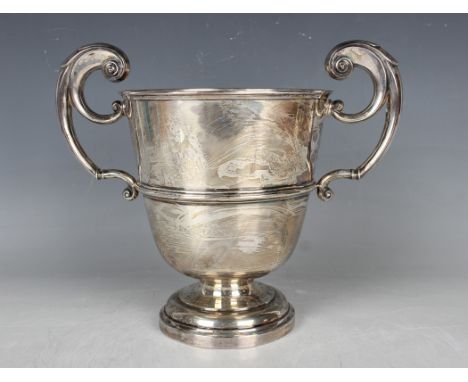 A George V silver trophy cup, the 'U' shaped girdled body flanked by a pair of flying scroll handles, on a circular domed foo