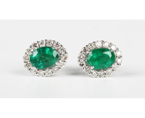 A pair of white gold, emerald and diamond oval cluster earstuds, each claw set with the oval cut emerald within a surround of