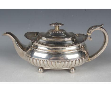 A George IV silver cushion shaped half-reeded teapot with floral decorated finial and foliate capped scroll handle, raised on