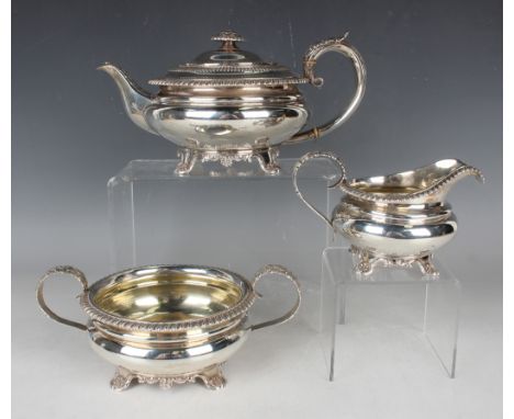 A George IV silver three-piece tea set, each piece of squat circular form with gadrooned rims, flanked by foliate capped scro