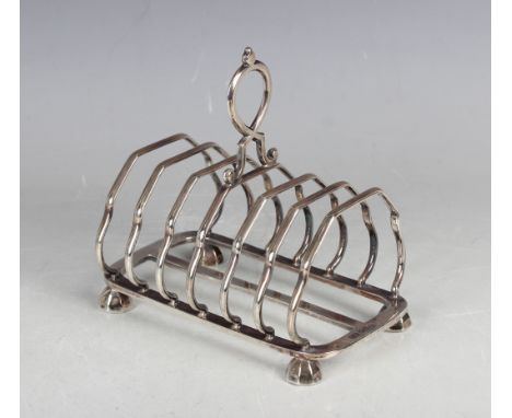 An Edwardian silver six-division toast rack with scroll handle, on faceted bun feet, Sheffield 1907 by Harrison Brothers &amp