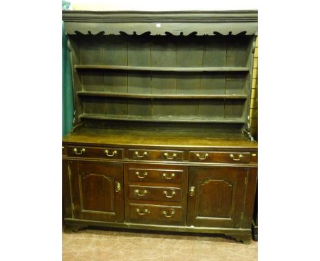 An 18th Century North Wales oak dresser, the three shelf wide boarded rack with shaped front frieze on a twin plank top over 