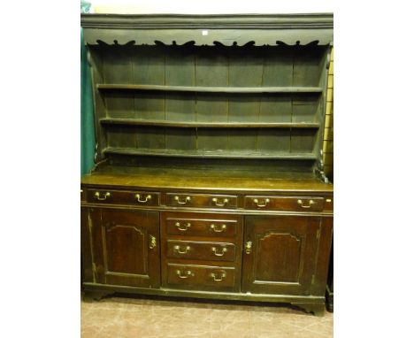 An 18th Century North Wales oak dresser, the three shelf wide boarded rack with shaped front frieze on a twin plank top over 