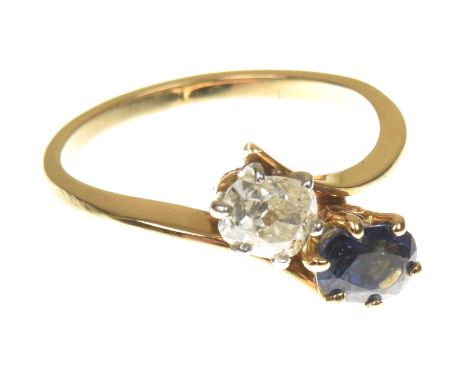 A sapphire and diamond crossover ringThe oval old cut diamond and sapphire duo, within a bi colour asymmetric setting, ring s