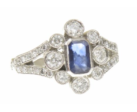 A sapphire and diamond cluster ringThe rectangular shape sapphire within a vari size brilliant cut diamond collet surround, a