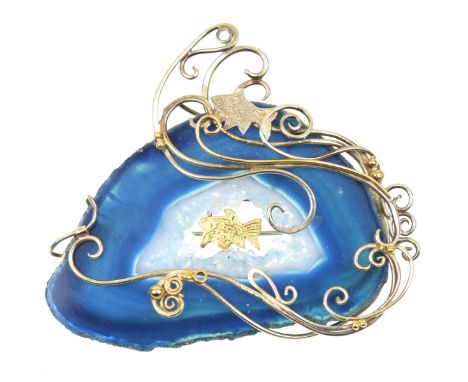 An agate and silver broochDesigned as a silver gilt fish within a freeform slice of dyed blue agate, and scrolling asymmetric