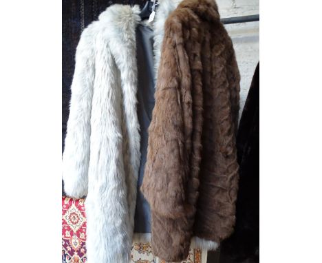 A lady's white and grey faux fur coat and a brown fur coat.