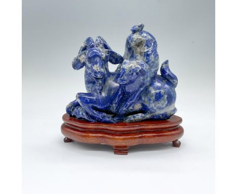 A blue and gray semi-precious stone carving on a young goat climbing over a resting adult goat with curved horns. This item h