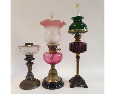 An oil lamp, with a cranberry glass shade, 63 cm high, another with a cranberry glass shade, 50 cm high and an oil lamp base 