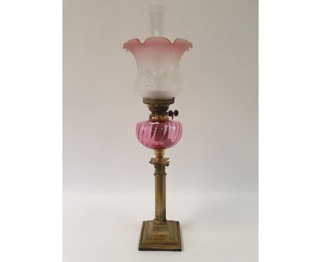 An oil lamp, with a cranberry tinted acid etched glass shade, a cranberry glass well, on a brass base in the form of a Corint