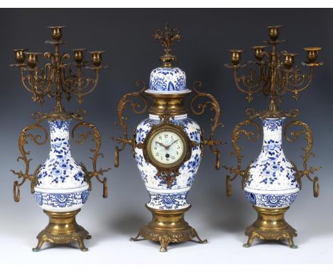 A clock garniture, the 8 cm diameter dial with Arabic numerals, in a pottery and gilt metal mounted case, 60 cm high, with a 