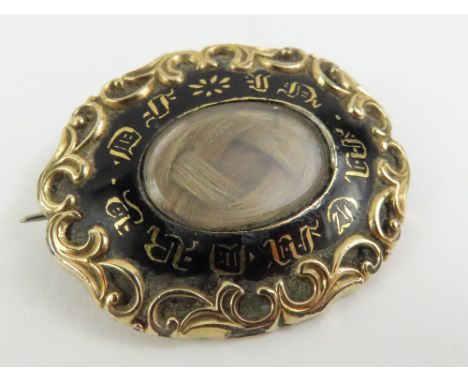 A 19th century mourning brooch, the front with hair panel and black enamel with gilt lettering around, and foliate border, to