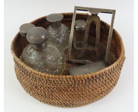 A small silver photo frame with easel back, silver topped dressing table jars and scent bottles contained in a woven basket