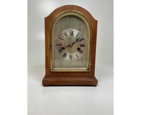 An Edwardian oak mantel clock, with arched case and silvered chapter ring with roman numerals.