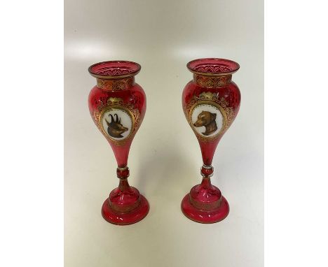 A pair of Victorian cranberry tinted Bohemian gilt heightened enamel decorated vases each set with opposing white enamel plaq