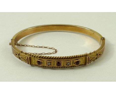 An Edwardian 9ct gold, diamond and ruby bangle, set with three rubies divided by two diamonds with rope twist border and bead