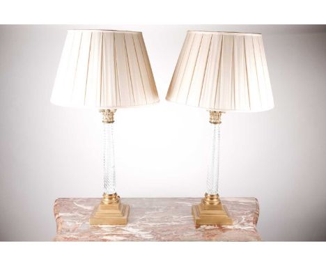 A pair of 20th-century brass and wrythen clear glass Corinthian column table lamps on stepped square bases, With ivory fabric