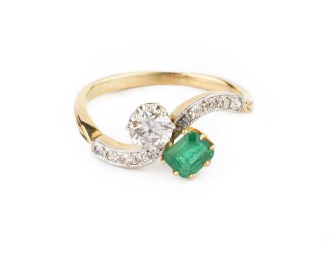 An emerald and diamond crossover ring, obliquely claw set with a rectangular step-cut emerald with canted corners and a round