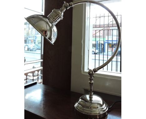 A plated desk lamp with circular shade on curved arm and stepped base.