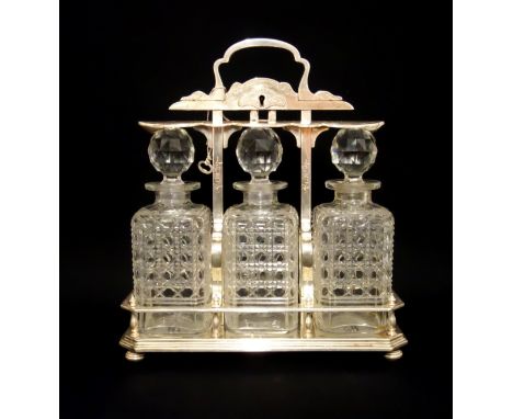 Victorian silver plated tantalus with chased decoration, the locking mechanism raising and lowering a bar over the decanters,