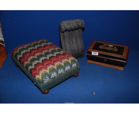 A small footstool with tapestry top and bun feet, vintage money tin and a black stone, scroll shaped, wall plinth.