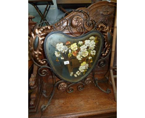 An Arts &amp; Crafts wrought iron framed firescreen having bronzed details, the shaped bevelled mirror painted with naturalis