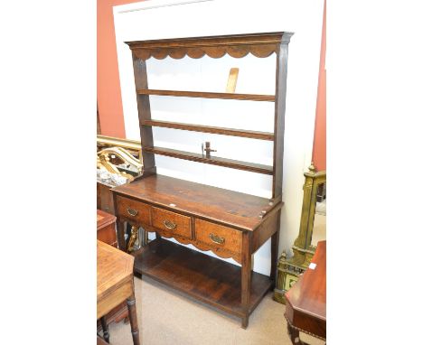 An oak dresser of small proportions with open four shelf plate rack above three drawers and square section supports united by
