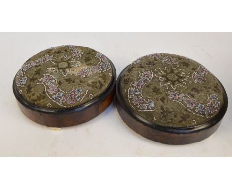 A pair of Victorian walnut circular bead work upholstered foot stools, on three ceramic bun feet.