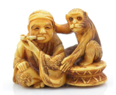 A Japanese Meiji period carved walrus tusk netsuke of a seated man smoking a pipe with a monkey, with incised and inked detai