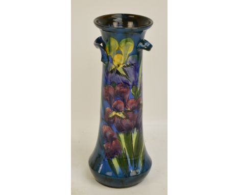 An early 20th century studio pottery vase of slender waisted form with stylised twin handles, floral hand painted on blue gro