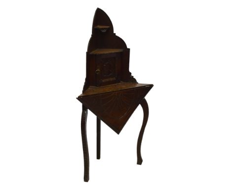 An early 20th century carved oak corner table with shaped back, small shelf above hinged door bearing carved bust panel above