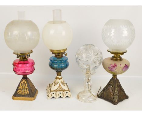 Three oil lamps with glass reservoirs on cast iron square section tapering bases, each with funnel and globular glass shade, 