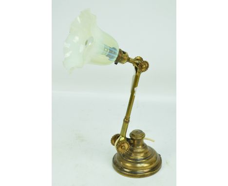 An early 20th century brass adjustable table lamp with weighted circular base, pivoting arm and vaseline tinted shade.
