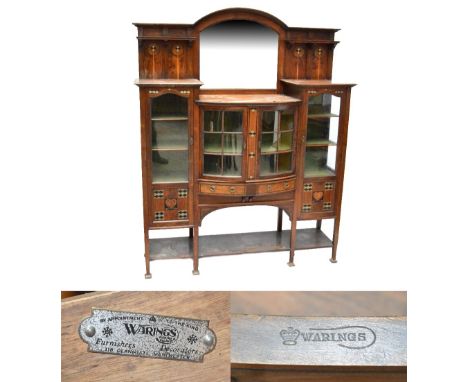 An Art Nouveau inlaid walnut display cabinet by Warings, with bevelled mirror back above central bowfront section with pair o