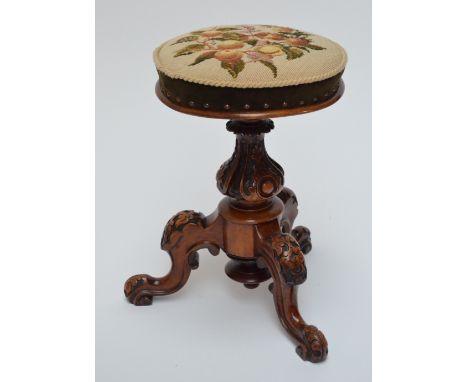 A Victorian walnut circular revolving piano stool with floral wool work upholstered seat above carved baluster column on thre