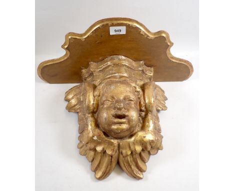 An antique gilt carved wood cherub mask wall bracket with later shaped shelf above, 31cm high 