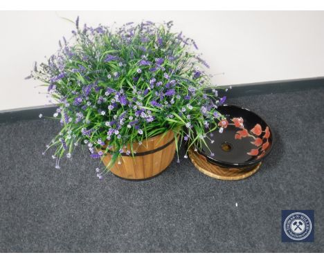 A barrel planter containing artificial plants and a black floral ceramic basin 
