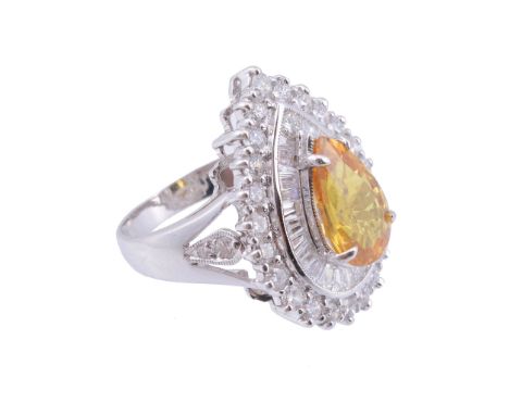  A yellow sapphire and diamond ring,   the central pear shaped yellow sapphire claw set within a surround of tapered baguette
