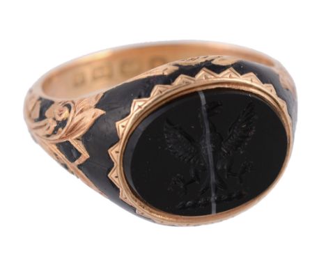  An 18 carat gold onyx signet ring,   the oval banded onyx carved with a crest, between foliate scroll black enamel shoulders