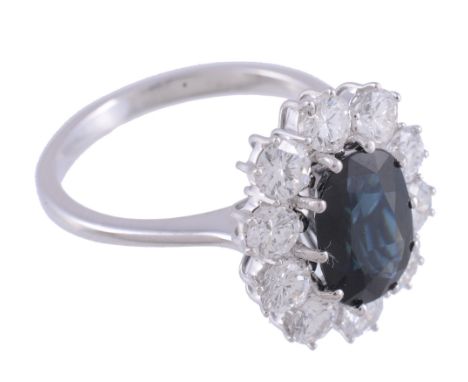  A sapphire and diamond cluster ring,   the central oval shaped sapphire claw set within a surround of brilliant cut diamonds