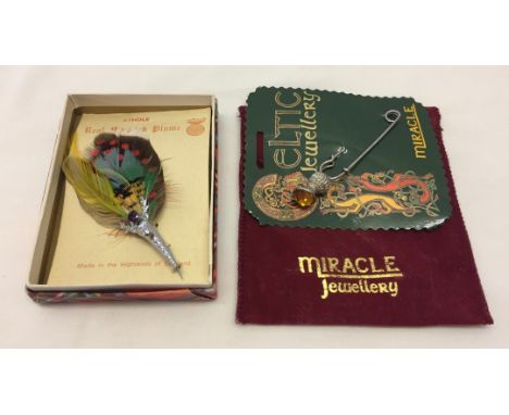 Comprising: a 'Real Scottish Plume' brooch in original box and a 'Miracle' celtic kilt pin/brooch in the original packaging. 